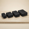 Bugatti set of 4 black compression packing cubes in graduated sizes on a neutral stone surface.